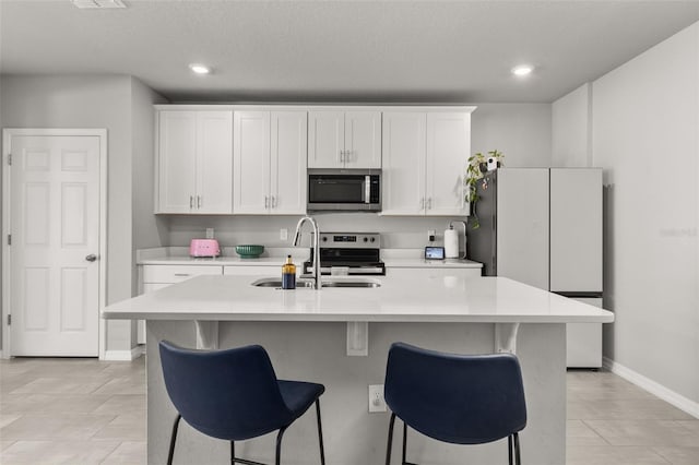 kitchen with sink, appliances with stainless steel finishes, white cabinets, and an island with sink