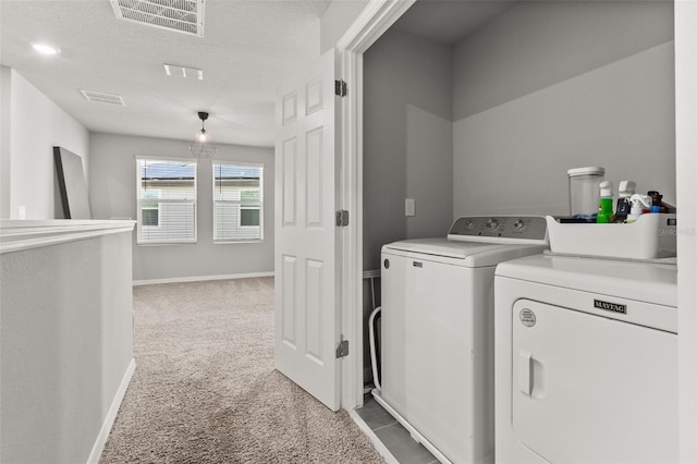 clothes washing area featuring a textured ceiling, washer and clothes dryer, and light colored carpet