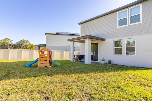 back of house featuring a lawn and a playground