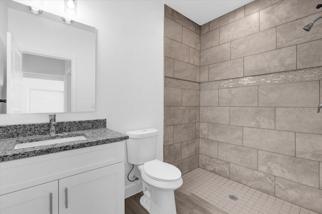 bathroom with toilet, hardwood / wood-style floors, vanity, and tiled shower