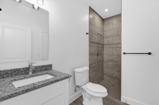 bathroom featuring toilet, vanity, wood-type flooring, and tiled shower