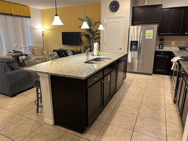 kitchen with a kitchen island with sink, a kitchen breakfast bar, sink, stainless steel fridge with ice dispenser, and decorative light fixtures