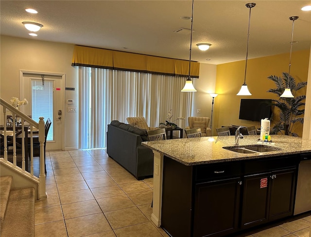 kitchen featuring light stone counters, sink, a center island with sink, and hanging light fixtures