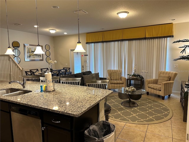 kitchen with light tile patterned floors, light stone countertops, stainless steel dishwasher, sink, and decorative light fixtures