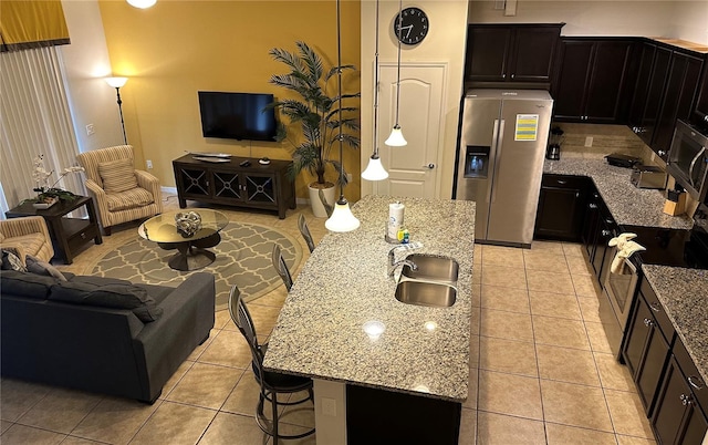 kitchen with a kitchen island with sink, a kitchen breakfast bar, sink, light stone countertops, and stainless steel fridge with ice dispenser