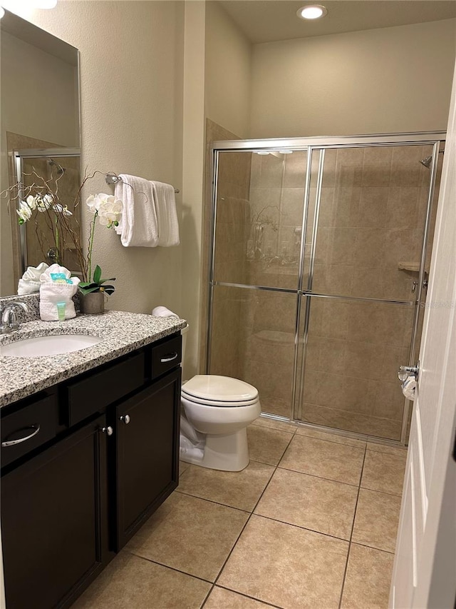 bathroom with toilet, a shower with shower door, vanity, and tile patterned floors