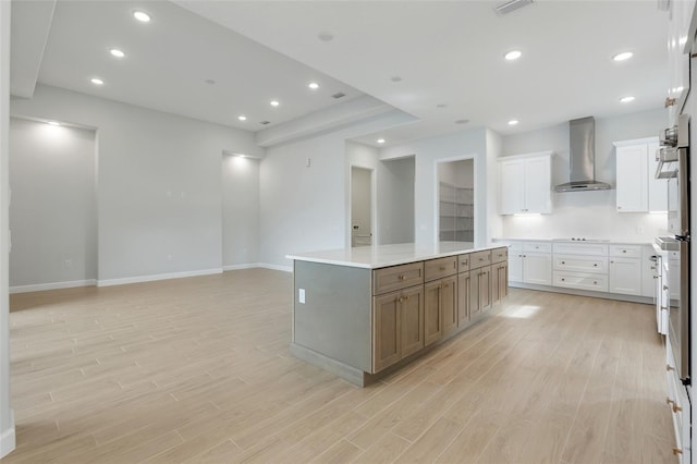 kitchen featuring a spacious island, light hardwood / wood-style floors, wall chimney exhaust hood, and white cabinets