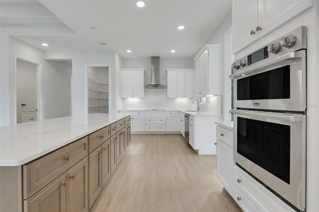 kitchen with white cabinetry, light hardwood / wood-style floors, stainless steel appliances, and wall chimney range hood