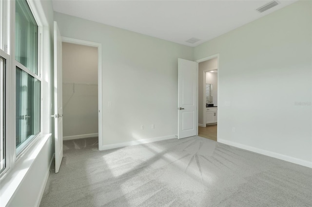 unfurnished bedroom featuring a closet, light carpet, and a walk in closet