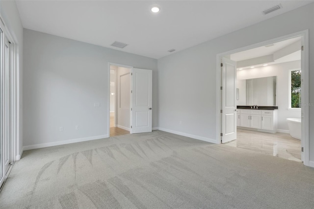 unfurnished bedroom featuring sink, light carpet, and ensuite bathroom