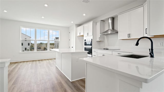 kitchen featuring light wood-style flooring, a kitchen island, light countertops, wall chimney range hood, and a sink