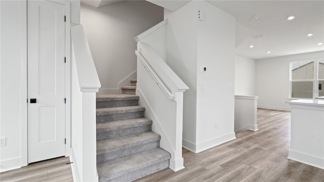 staircase featuring baseboards, wood finished floors, and recessed lighting