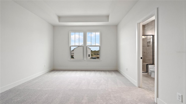 unfurnished bedroom featuring ensuite bath, baseboards, a tray ceiling, and carpet flooring