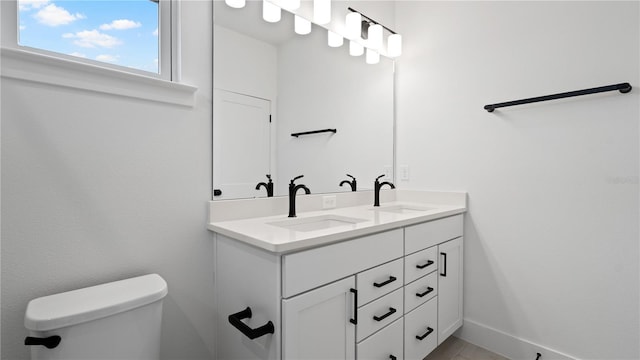 full bathroom featuring double vanity, a sink, toilet, and baseboards