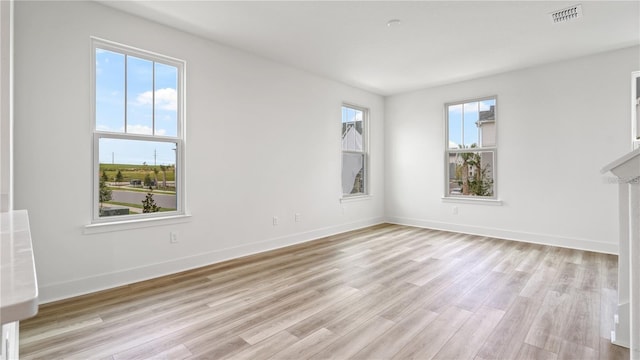 empty room with light wood finished floors, baseboards, and visible vents