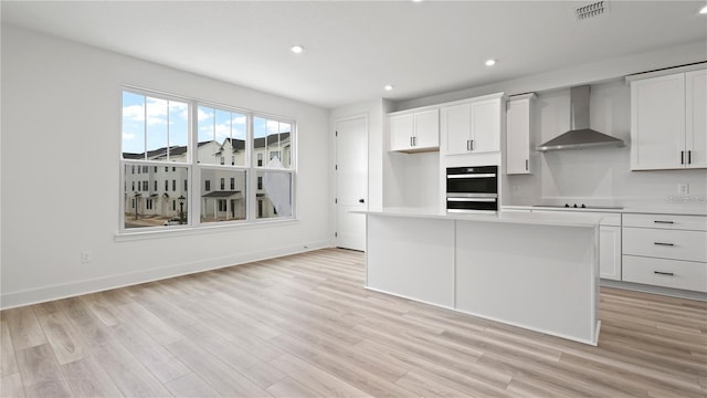 kitchen with black electric cooktop, visible vents, white cabinetry, light countertops, and wall chimney range hood