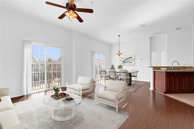 living room featuring a ceiling fan, visible vents, baseboards, and wood finished floors