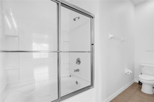 bathroom with baseboards, bath / shower combo with glass door, toilet, and tile patterned floors