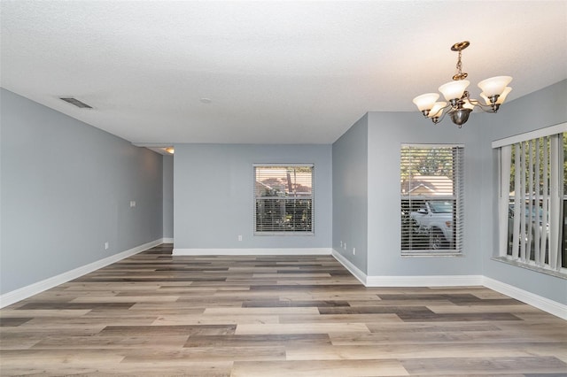 empty room with hardwood / wood-style floors, a textured ceiling, and a notable chandelier