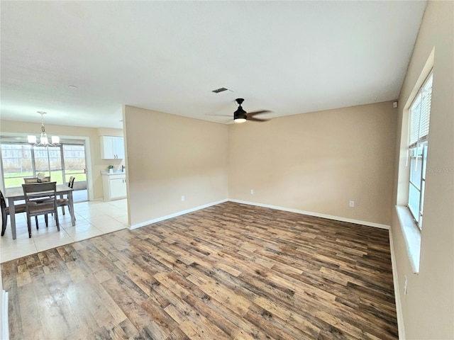 spare room featuring ceiling fan with notable chandelier and light wood-type flooring