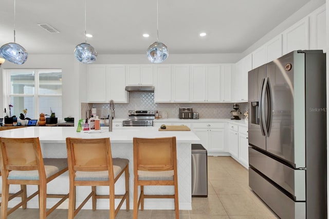 kitchen with appliances with stainless steel finishes, white cabinets, a kitchen island with sink, and pendant lighting