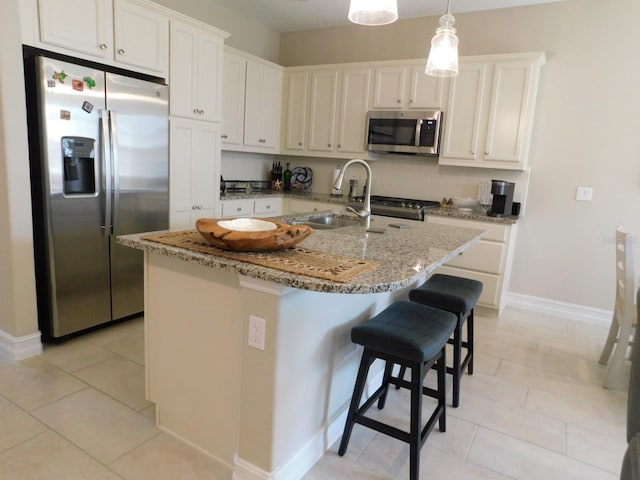 kitchen featuring a kitchen island with sink, hanging light fixtures, light stone countertops, white cabinetry, and appliances with stainless steel finishes