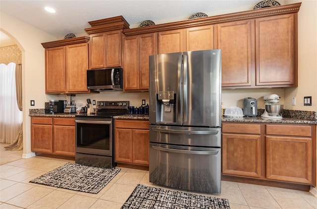 kitchen featuring vaulted ceiling, appliances with stainless steel finishes, dark stone counters, and light tile patterned flooring