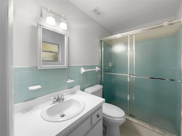 bathroom with tile walls, vanity, toilet, and an enclosed shower