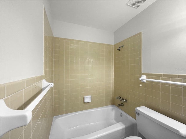 bathroom featuring tiled shower / bath, tile walls, and toilet