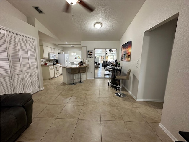 interior space with white appliances, a kitchen bar, a textured ceiling, white cabinetry, and lofted ceiling