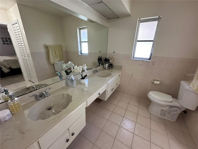 bathroom with vanity, toilet, tile walls, and tile patterned flooring