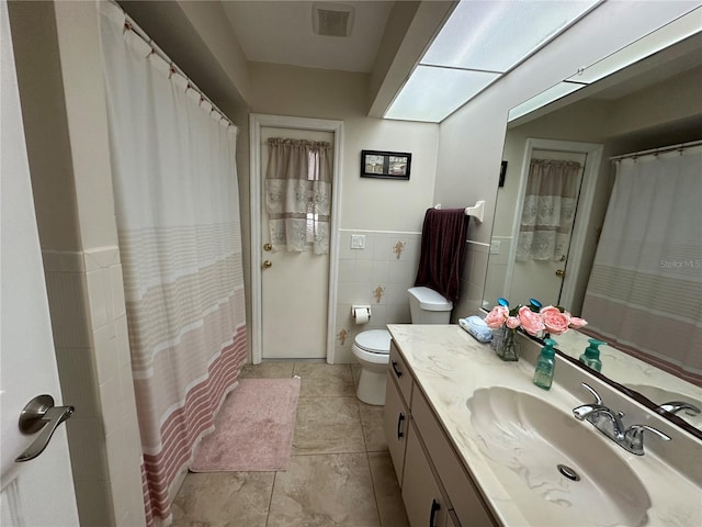 bathroom with toilet, tile patterned flooring, vanity, curtained shower, and tile walls