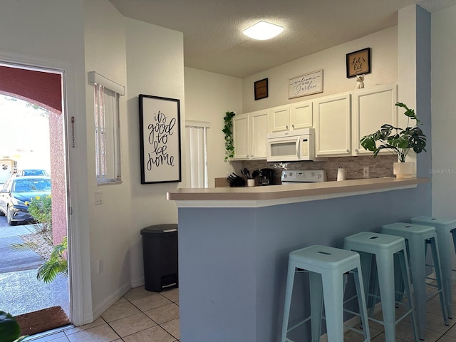 kitchen featuring white appliances, tasteful backsplash, kitchen peninsula, white cabinetry, and a breakfast bar area