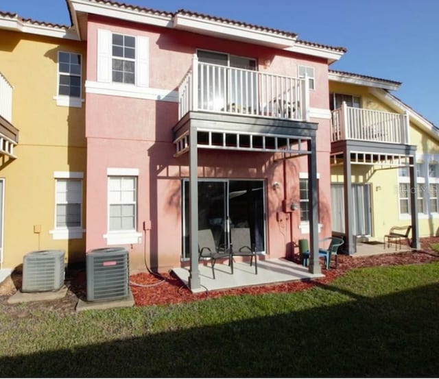 rear view of property featuring central AC unit, a lawn, a patio, and a balcony