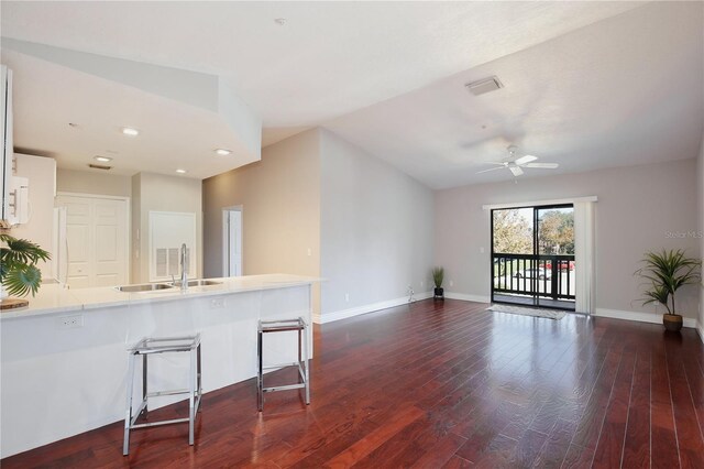 kitchen with a kitchen bar, kitchen peninsula, ceiling fan, sink, and dark hardwood / wood-style floors