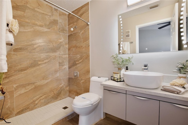 bathroom featuring a tile shower, ceiling fan, hardwood / wood-style floors, toilet, and vanity