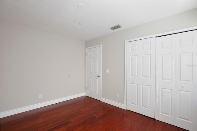 unfurnished bedroom with dark hardwood / wood-style flooring, a textured ceiling, and a closet