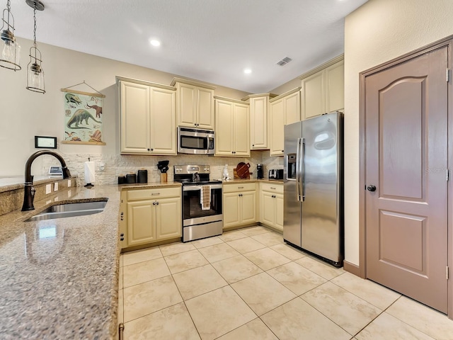 kitchen featuring appliances with stainless steel finishes, light stone counters, sink, cream cabinets, and decorative light fixtures