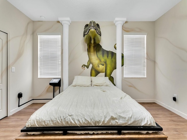 bedroom featuring light hardwood / wood-style floors, multiple windows, and decorative columns