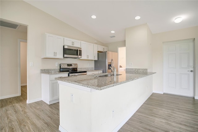 kitchen featuring white cabinetry, appliances with stainless steel finishes, vaulted ceiling, kitchen peninsula, and light hardwood / wood-style flooring