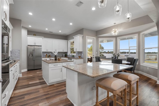 kitchen with an island with sink, stainless steel appliances, white cabinetry, and tasteful backsplash