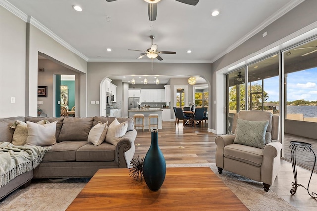 living room with ornamental molding, ceiling fan, light wood-type flooring, and plenty of natural light