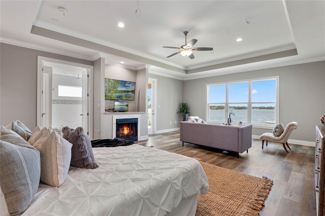 bedroom with crown molding, hardwood / wood-style flooring, a tray ceiling, and ceiling fan