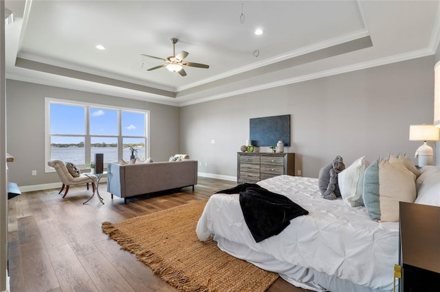 bedroom featuring a water view, hardwood / wood-style flooring, a tray ceiling, and ceiling fan