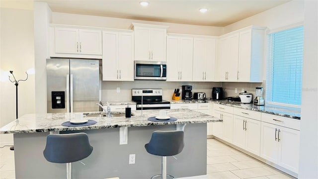 kitchen with white cabinets, stainless steel appliances, a center island with sink, and a breakfast bar area