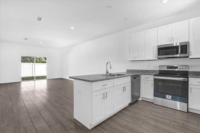 454 Lake Shore Pkwy, Davenport, FL 33896 - kitchen with stainless steel appliances, a sink, a peninsula, white cabinets, and dark stone countertops