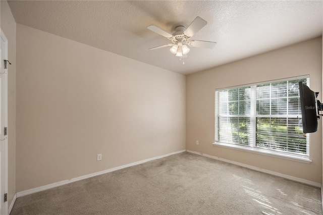 unfurnished room featuring baseboards, light colored carpet, a ceiling fan, and a textured ceiling