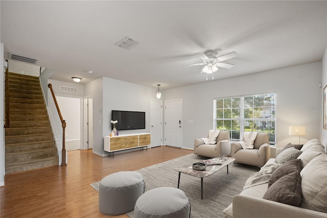 living room featuring ceiling fan, visible vents, wood finished floors, and stairway