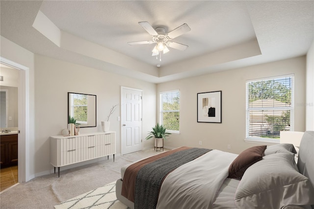 bedroom featuring a tray ceiling, multiple windows, light colored carpet, and baseboards