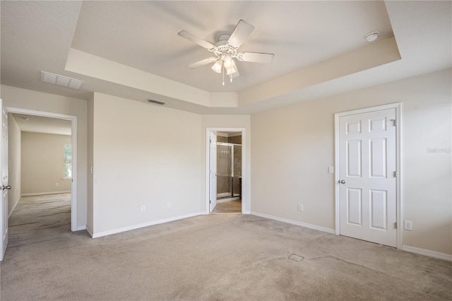 unfurnished bedroom featuring a tray ceiling, light colored carpet, and visible vents